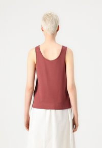 Top de tanque burdeos hecho de tela suave, con un escote en la espalda y tirantes anchos, combinado con una falda blanca. Textura suave, diseño casual.