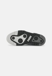 Svart og grå sneaker yttersåle med teksturert gummi, kontrasterende hvite detaljer, sirkulære dekkmønstre og merkevaren logo tydelig vist.