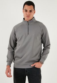 Šedý mikinový svetr s půlzip límcem, raglánovými rukávy a žebrovanými manžetami. Na hrudi se nachází jednoduché logo, vyrobený z měkkého materiálu.