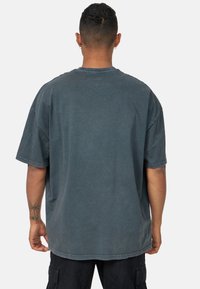 Camiseta de algodón oscura de gran tamaño y mangas cortas, con un acabado desgastado, escote redondo y costuras visibles en los bordes.