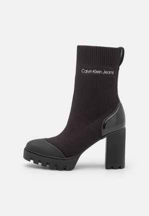 Sort sokkelignende ankelstøvle med chunky høj hæl, grov sål, ribbet manchet og "Calvin Klein Jeans"-logo på strikket overdel.