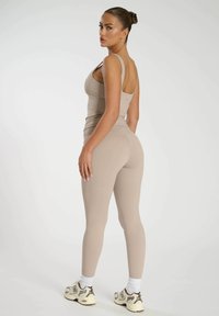 Beige atletisk linne och leggings, åtsittande, med slät yta och minimala sömmar. Modell som bär sneakers med tonala accenter.