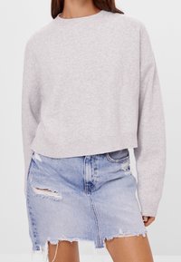 Suéter corto gris claro con dobladillo acanalado y hombros caídos, combinado con una falda de denim desgastada que presenta bordes deshilachados y múltiples roturas.