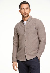 Camicia marrone con bottoni, realizzata in tessuto testurizzato, dotata di tasca sul petto e maniche lunghe, con bottoni scuri e una vestibilità sartoriale.