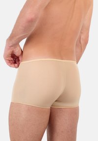 Boxer da uomo beige, design aderente, texture liscia, cuciture sottili lungo l'elastico in vita e taglio stile shorts, visibili sulla schiena di un modello.