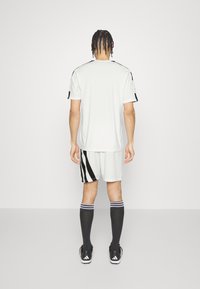 Vit sporttröja med svarta accenter, kombinerad med vita shorts med svarta ränder. Svarta strumpor och skor avslutar outfiten.
