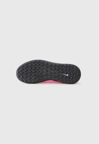 Sorte gummisåle med teksturert gripe mønster og liten hvit Nike swoosh logo, sett fra bunnen mot en ensfarget bakgrunn.
