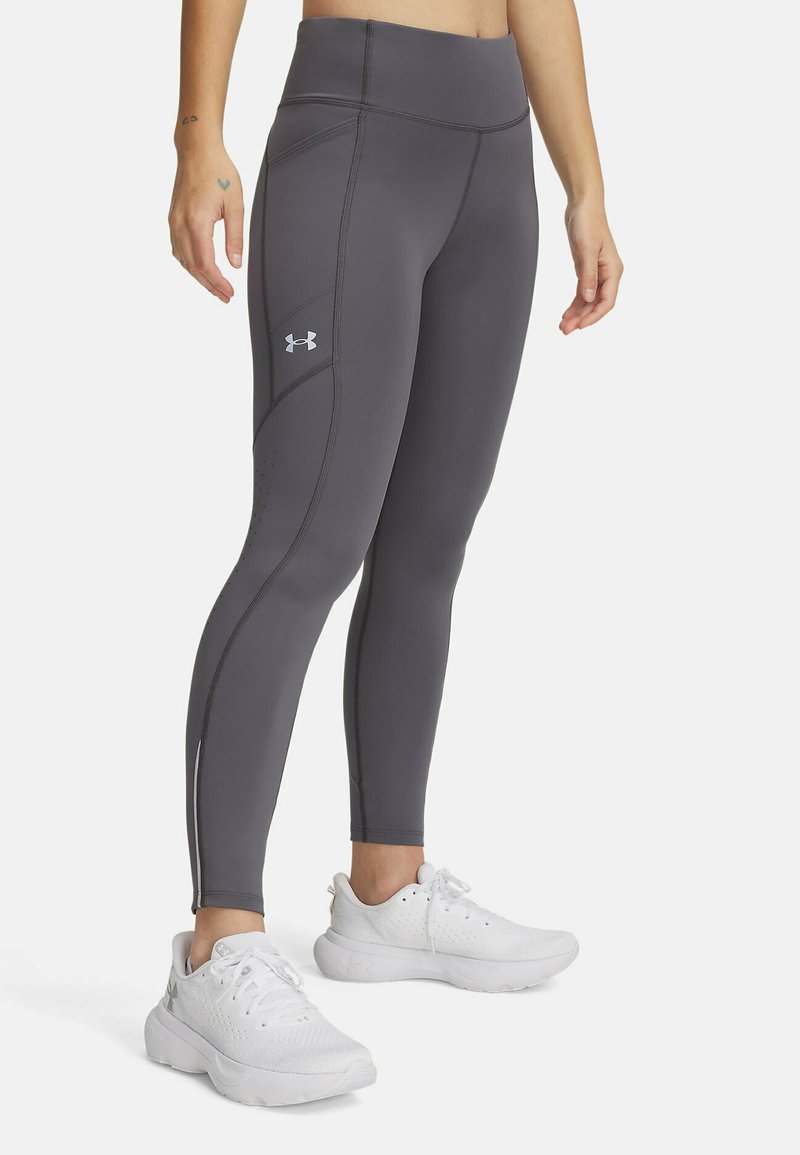 Leggings de sport gris avec une taille haute, présentant des détails de couture subtils et un petit logo. Portés avec des sneakers blanches.
