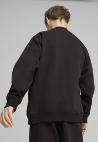 Czarny sweter z okrągłym dekoltem, z prążkowanymi mankietami i dołem. Gładka tekstura, luźny krój, bez widocznych wzorów czy logotypów.