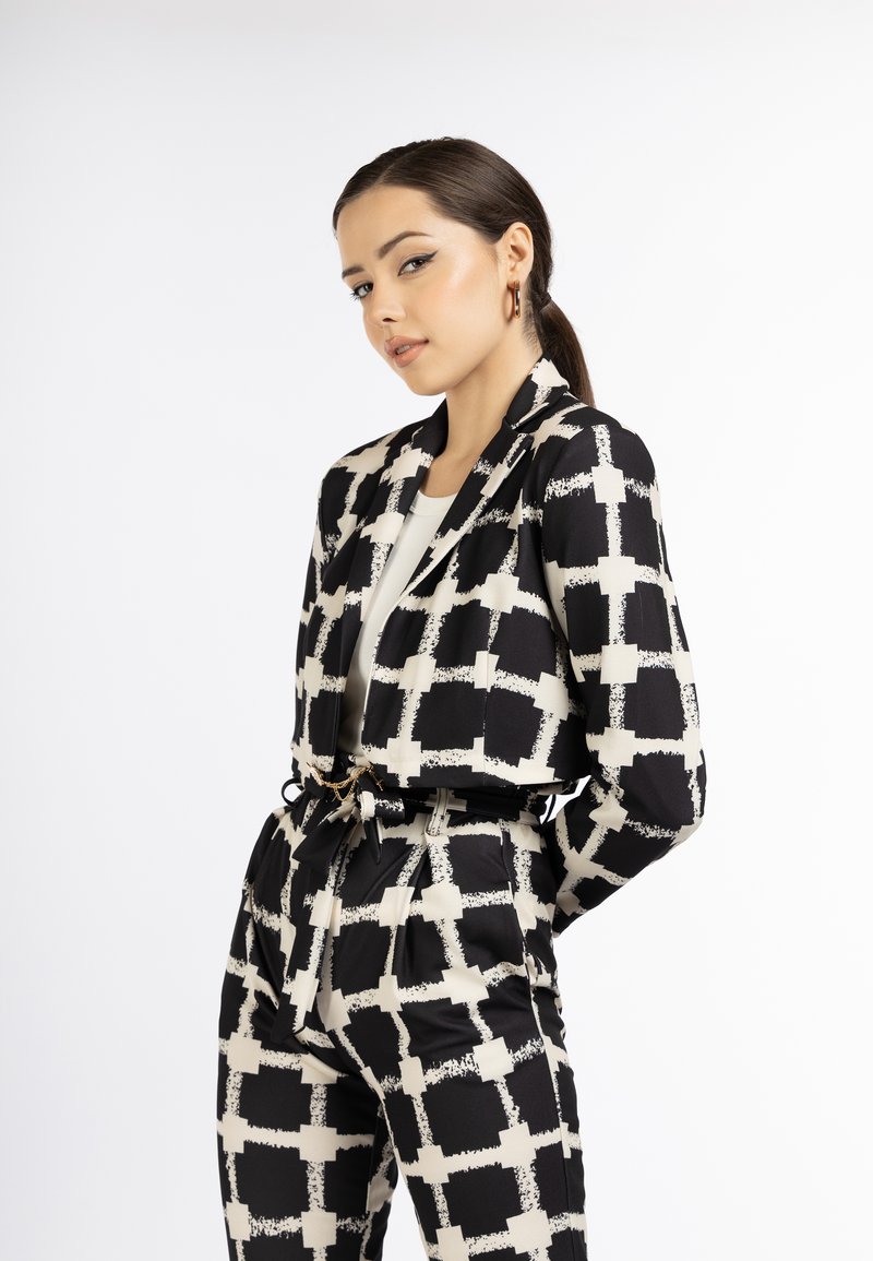 Zwart-wit blazer en broek set met een geometrisch patroon. Gemaakt van een gladde stof met een gestrikt ceintuur en details van voorzakken.