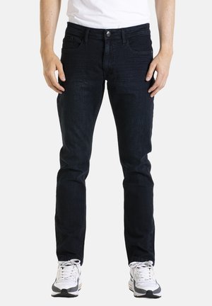 Jean en denim noir avec une coupe slim, dotés de cinq poches, d'une fermeture à bouton et d'un léger délavage à l'avant. Portés avec des chaussures de sport blanches.