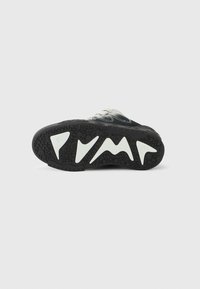 Μαύρη σόλα αθλητικού παπουτσιού με λευκά γεωμετρικά σχήματα και υφή για καλύτερη πρόσφυση, εμφανιζόμενη από κάτω σε λευκό φόντο.