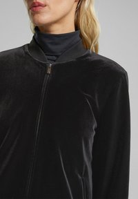 Czarna aksamitna kurtka bomber z zapięciem na suwak i prążkowanym kołnierzem. Gładka tekstura i dopasowany krój, bez widocznych logo ani wzorów.