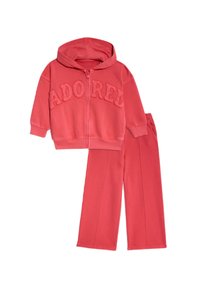 Korálově růžová mikina na zip s vyšitým nápisem "ADORED" v čalouněném písmu, spárovaná s odpovídajícími tepláky s postranními švy a elastickým pasem.