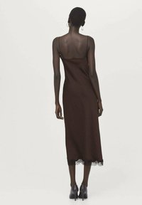 Bruine slipjurk met spaghetti bandjes, voorzien van een kanten rand aan de zoom. Soepele stof, tot halverwege de kuit en een aansluitend silhouet.