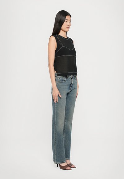 Top sans manches noir avec des coutures blanches contrastantes, associé à un jean bleu clair à jambe droite et des sandales à talons marron.