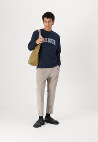 Ναυτικό sweatshirt με τη λέξη "HARBOUR" σε λευκό χρώμα, μπεζ παντελόνι καμπάνα από κοτλέ και μαύρα παντόφλες; το μοντέλο κρατάει μια καφέ τσάντα tote.