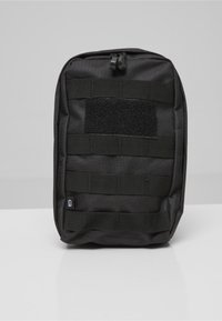 Bolsa táctica negra con correas de tejido horizontales y un parche grande de gancho y bucle en la parte frontal, sobre una superficie blanca.