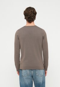 Brązowa, dopasowana bluzka z długim rękawem wykonana z prążkowanej tkaniny, z okrągłym dekoltem i minimalnymi detalami szwów, zestawiona z jasnoniebieskimi dżinsami.