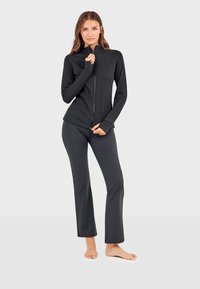 Crna atletska jakna sa dugim rukavima i otvorima za palceve, uparena sa prilagođenim crnim hlačama. Glatka tekstura i aerodinamičan dizajn.