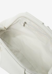 Interno di una borsa bianca con fodera in tessuto liscio, dotata di una tasca con cerniera e un'etichetta. La forma complessiva è leggermente rettangolare.