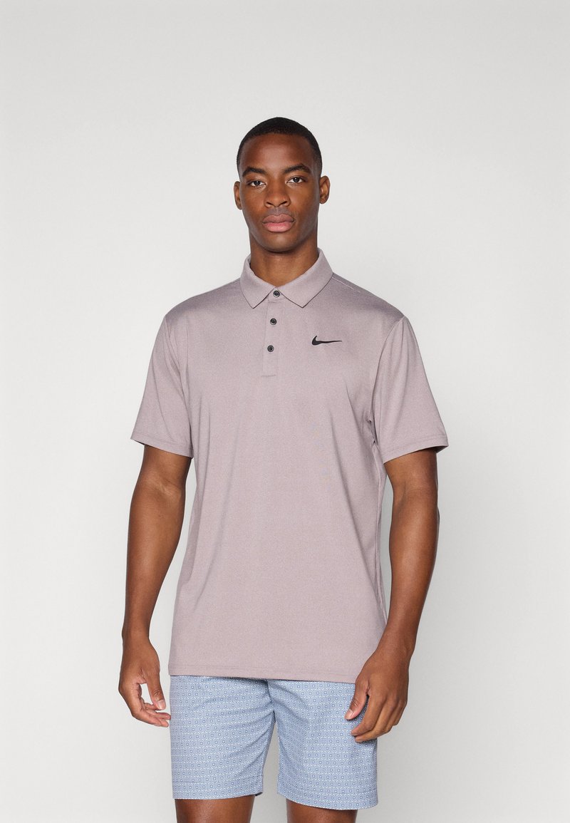 Hnedý polo tričko s krátkym rukávom a golierom, so zapínaním na tri gombíky a čiernym logom Nike na ľavej hrudi, nosené s modrými vzorovanými šortkami.