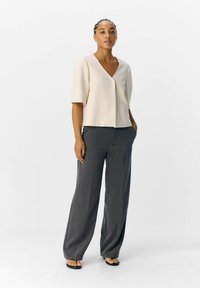 Haut de couleur claire à manches courtes avec un col en V, associé à un pantalon taille haute à jambes larges de couleur gris foncé et des sandales plates.