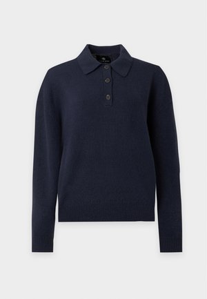 Kvinde iført en mørk langærmet polo sweater, ternet mini nederdel og bordeaux Mary Jane sko står foran en ensartet lys baggrund.