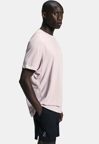 Lyserød atletisk t-shirt med korte ærmer, rund halsudskæring og diskret branding. Matchet med sorte shorts med logodetalje.