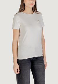 T-shirt di cotone grigio chiaro con maniche corte e scollo rotondo. Presenta un piccolo logo triangolare sul petto. Design aderente.