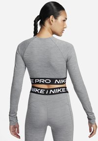 Camiseta atlética de manga larga en tela gris claro con textura acanalada, que cuenta con una cinturilla con logo negro y mangas raglán para una mejor movilidad.