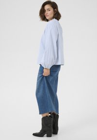 Blouse à manches bouffantes rayée bleu clair et blanche, associée à une jupe en denim bleu foncé et des bottes de cowboy noires, offrant une coupe décontractée.
