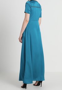 Teal maxi dress with short sleeves, featuring a smooth texture and delicate detailing along the shoulders. Floor-length silhouette.