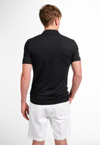 Sort kortærmet polo med ribbet krave, båret med hvide shorts. Stoffet ser glat ud, med en tætsiddende pasform og minimale sømme.