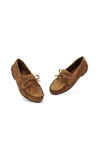 Mocasines de ante marrón con puntera redondeada, detalles de costura y cierre con cordones. Textura suave y suela de goma minimalista.