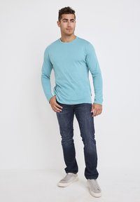  Lichtblauwe lange mouwen shirt van katoen, gecombineerd met donkerblauwe denim jeans en grijze sneakers. Eenvoudig ontwerp, casual pasvorm.