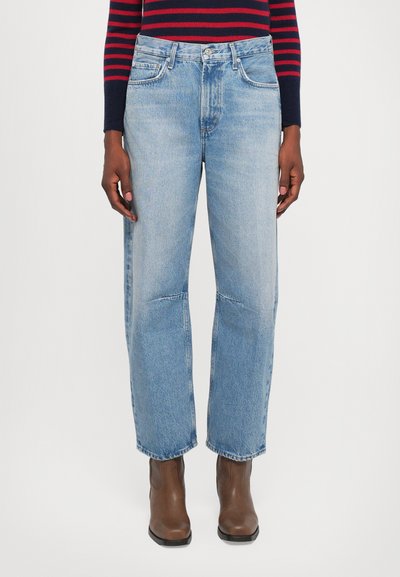 Jeans in denim blu chiaro con un design a gamba dritta, dotati di tasche frontali, passanti per cintura e dettagli di cucitura visibili. Indossati con stivali alla caviglia marroni.