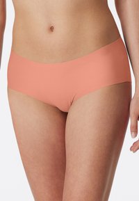 Hipster-trusser i ferskenfarve lavet af glat, elastisk stof. Har et sømløst design, talje i midterhøjde og fuld dækning.