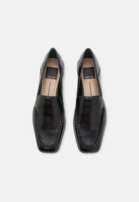 Chaussures en cuir noir avec un bout carré, texture lisse et coutures visibles. L'intérieur présente une semelle intérieure de marque. Design élégant.