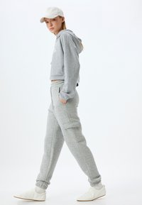 Grijze cropped hoodie met geborduurd detail, gecombineerd met bijpassende grijze sweatpants met zijzakken en manchetten. Witte sneakers.