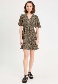 Robe imprimée léopard avec un décolleté en V, des manches courtes et une taille élastique, présentant un ourlet évasé. Associée à des sandales noires épaisses.