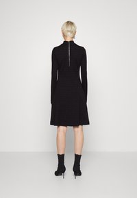 Robe noire à manches longues avec corsage ajusté et jupe évasée. Présente un col montant et une fermeture éclair apparente dans le dos. Texture de tissu lisse.