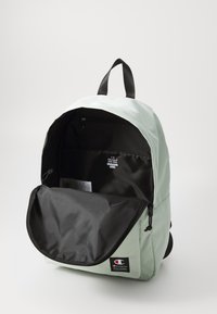 Sac à dos vert menthe avec une finition lisse. Dispose d'une poche zippée noire et d'un grand compartiment principal. Bandoulières noires et patch logo à l'avant.