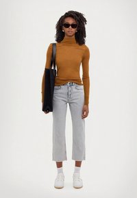 Ruosteenvärinen pitkähihainen poolopaita, vaaleanharmaat korkeavyötäröiset lyhytlahkeiset farkut, valkoiset tennarit, musta olkalaukku ja mustat aurinkolasit. Yksivärinen tausta.