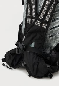 Rucsac negru realizat din material mesh, cu curele reglabile și o cataramă din plastic. Include accente texturate și buzunare laterale pentru depozitare.