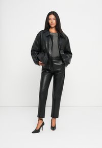Veste en cuir noir, top gris ajusté, pantalon en cuir noir cintré et chaussures à talons hauts noires. Design simple avec une texture lisse.