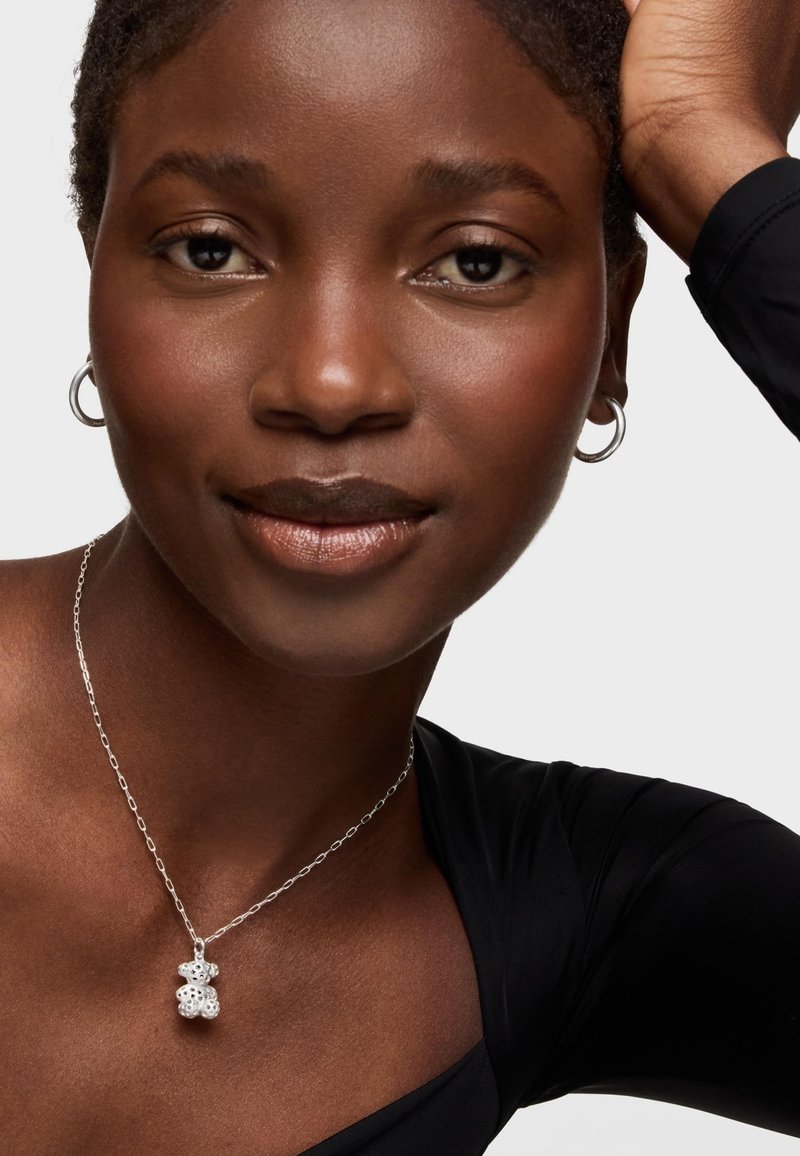 Pendentif en argent représentant un ours, avec une chaîne à maillons, porté sur un haut noir. Textures lisses et finition polie.