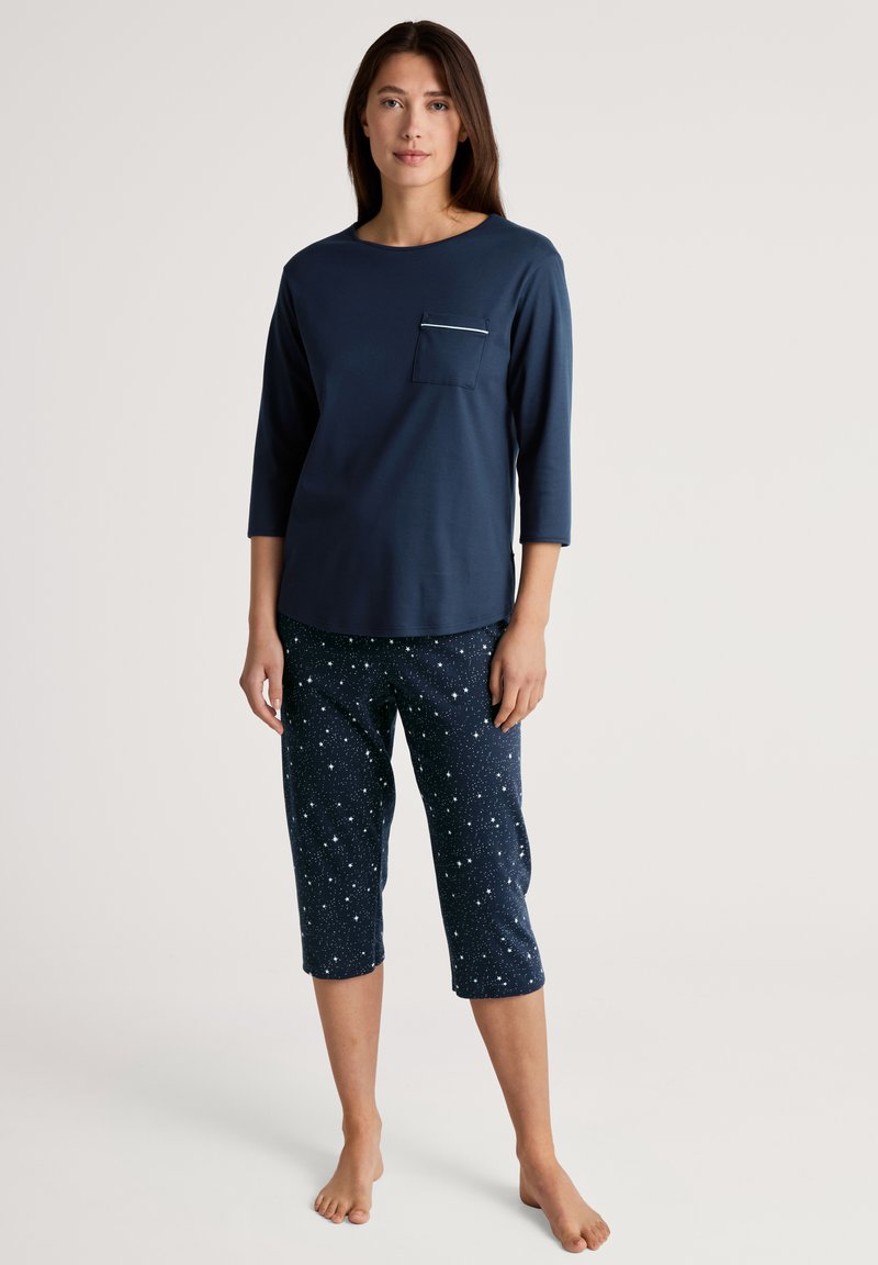Marineblauw shirt met driekwart mouwen en een borstzak; gecombineerd met marineblauwe pyjamabroeken met een wit sterpatroon. Gemaakt van zacht katoen.