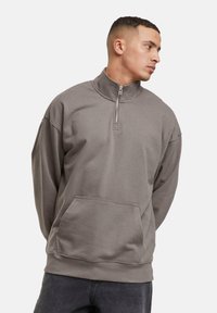 Sweatshirt zippé gris avec un col montant, poche avant, coupe décontractée et texture douce. Comprend des poignets et un ourlet côtelés.