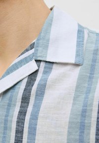 Maglietta a righe con diverse tonalità di blu e bianco. Tessuto leggero, colletto alla francese e texture delicata con righe orizzontali ben visibili.